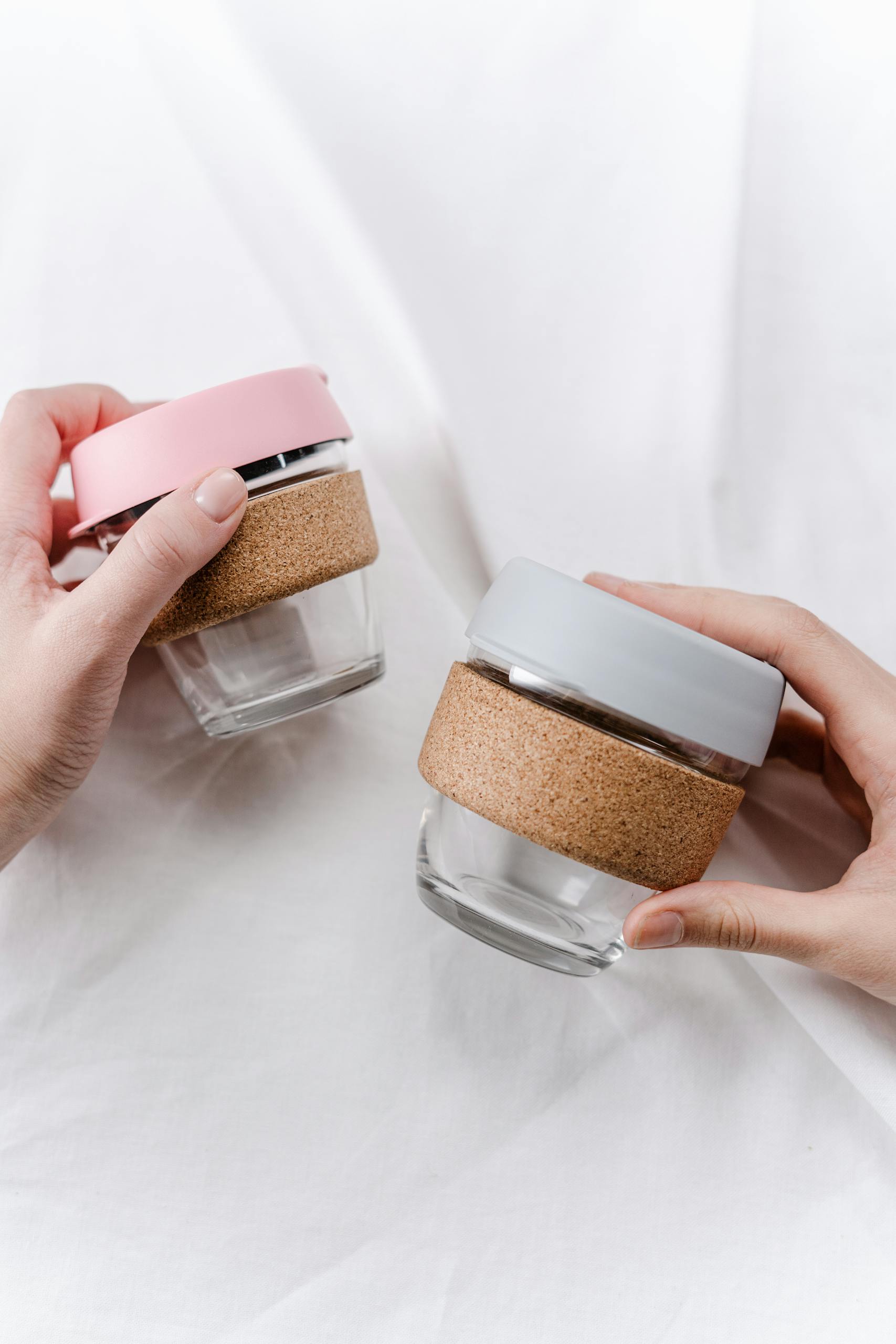 Close-up of hands holding eco-friendly glass cups with cork and silicone lids.