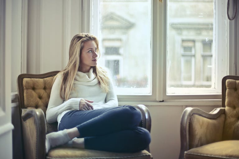 A serene moment of a woman in a cozy room, enjoying leisure time by the window.