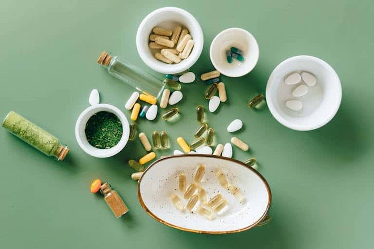 Top view of various herbal and pharmaceutical supplements in ceramic bowls on a green background.