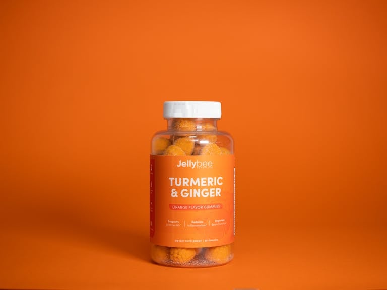 Bright image of Jellybee Turmeric & Ginger gummies in a plastic bottle against an orange backdrop.